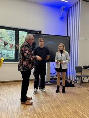 Ein älterer Mann spricht freundlich mit einer jungen Frau und einem jungen Mann in heller moderner Umgebung